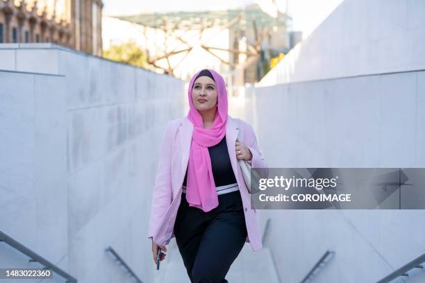 young arabic woman with pink veil going up some stairs looking up. - middle east business people stock pictures, royalty-free photos & images