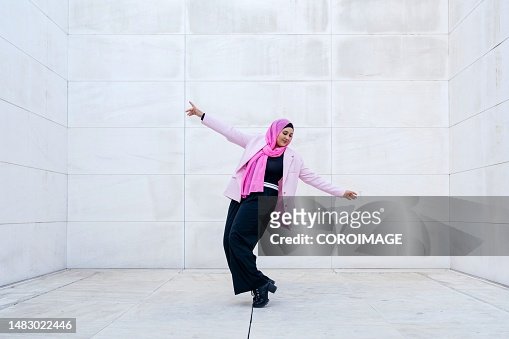Young Muslim woman dancing with arms raised.