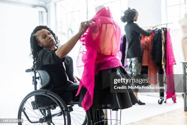 female fashion designer in wheelchair adjusting clothing on dress form - handicap photos et images de collection