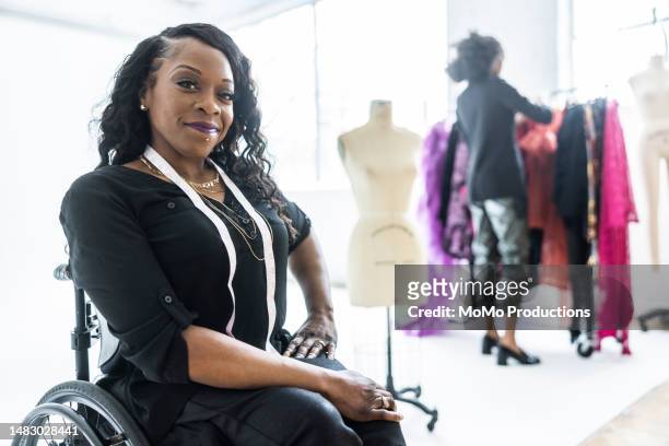 portrait of female fashion designer in wheelchair in front of clothing racks in photo studio - sia - fotografias e filmes do acervo