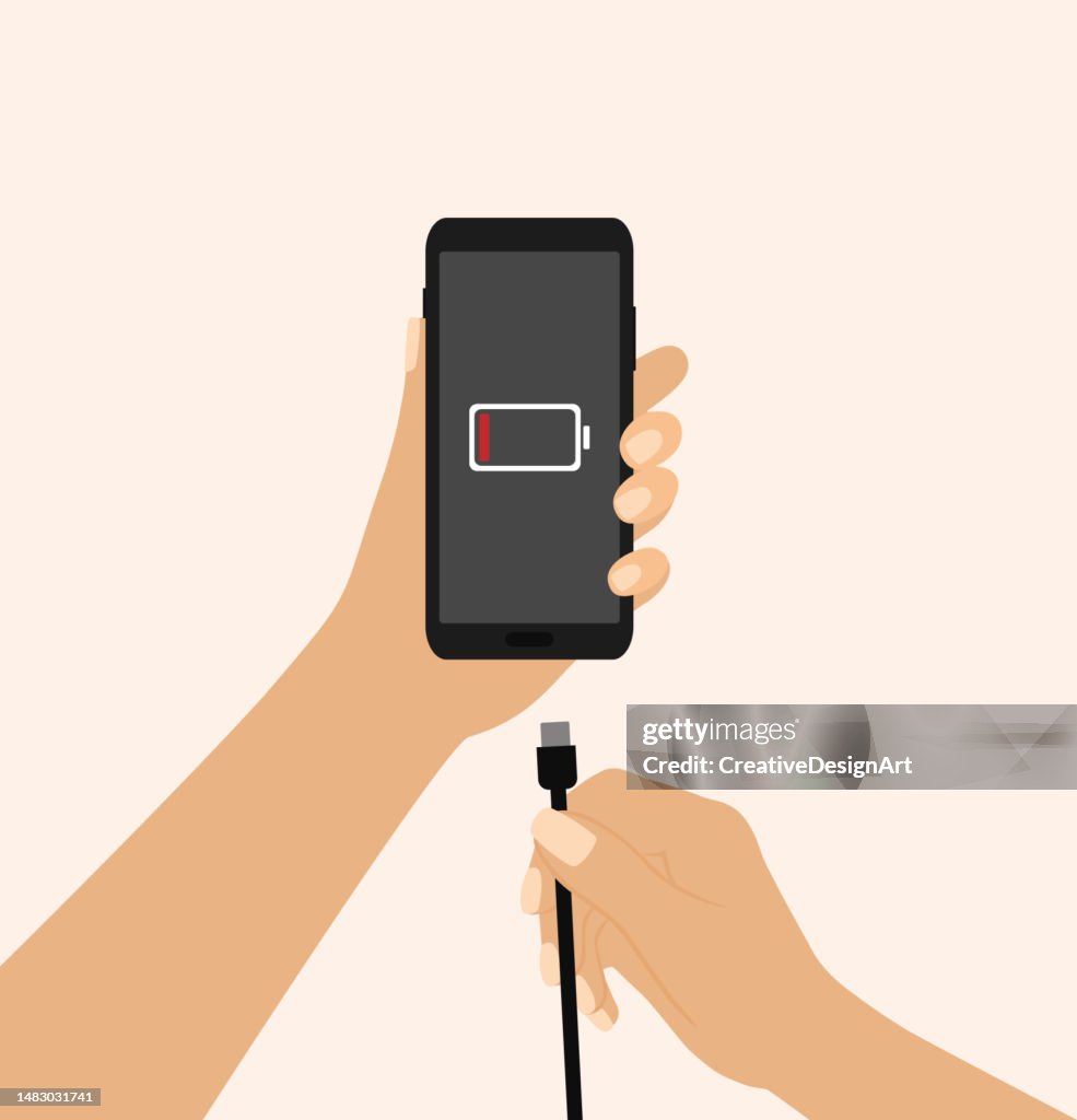 Hand Holding A Mobile Phone And Charger. Low Battery Symbol On Phone Screen