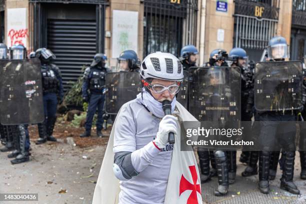 Manifestant avec une cape avec croix rouge des templiers parlant au micro de suicide devant un cordon de policiers anti-émeute lors de la...