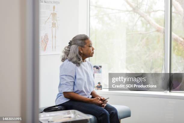 la donna matura tiene il suo telefono cellulare e aspetta il medico - risultati di esami medici foto e immagini stock