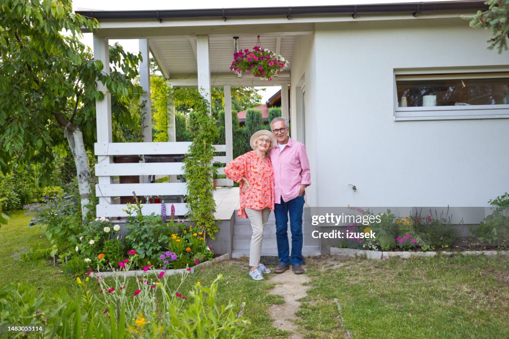 Smiling senior couple standing outside house