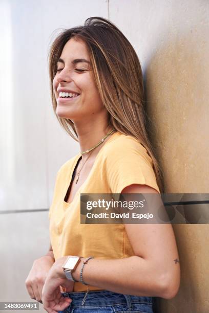 young woman with eyes closed smiling while leaning on a wall. - woman smiling eyes closed stock pictures, royalty-free photos & images