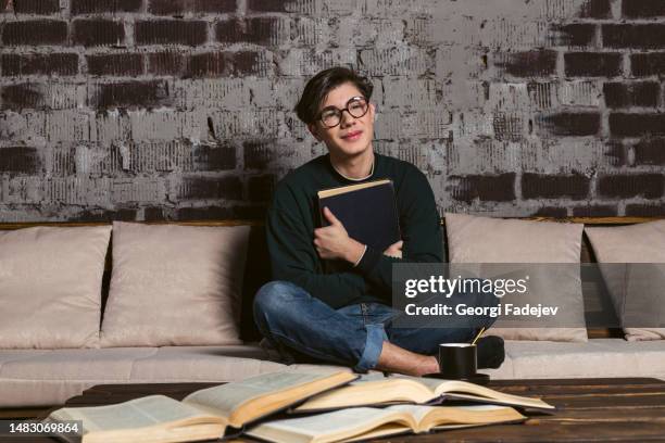 a hard learning student dressed neatly, in round glasses is reading and studying among piles and stacks of books. - book nerd stock pictures, royalty-free photos & images
