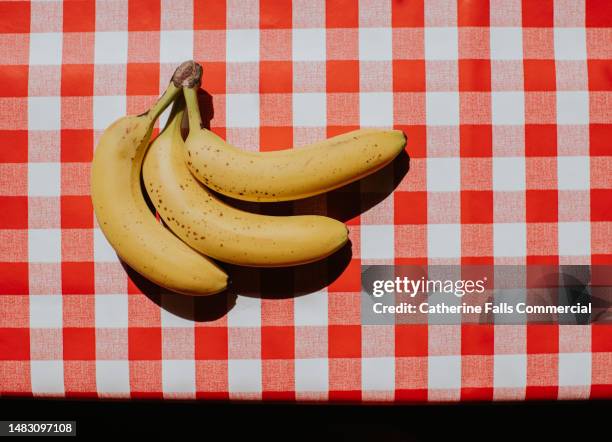 bright, graphic, simple image of three bananas on a red checkered tablecloth - three objects stock pictures, royalty-free photos & images