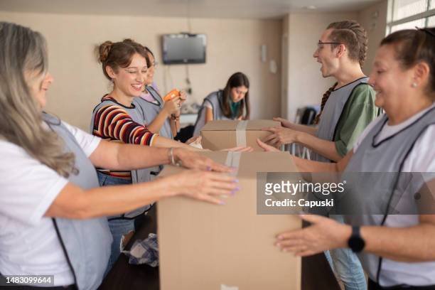 volunteers closing boxes with tape - clear donation box stock pictures, royalty-free photos & images
