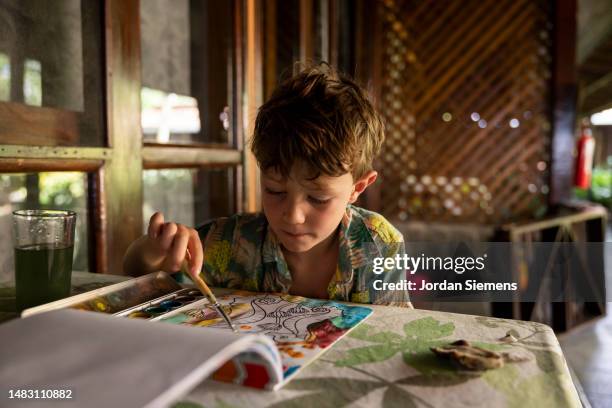 a young boy painting in a coloring book while on vacation. - summer coloring stock pictures, royalty-free photos & images