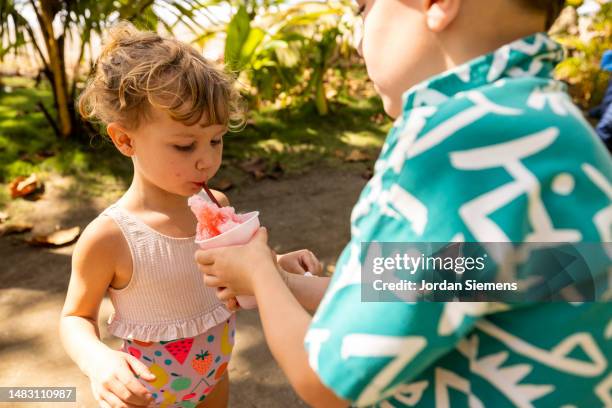 a boy and a girl sharing a shaved ice on a hot day. - sisters feeding stockfoto's en -beelden