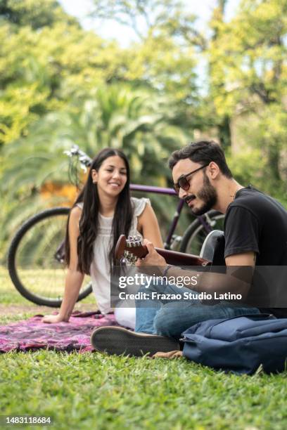 giovane che canta mentre suona la chitarra acustica alla sua ragazza nel parco pubblico - cantare una serenata foto e immagini stock