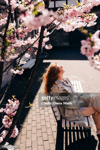 happy woman with red hair enjoying sunny spring day at the city under the blossoming tree - hanover stock pictures, royalty-free photos & images