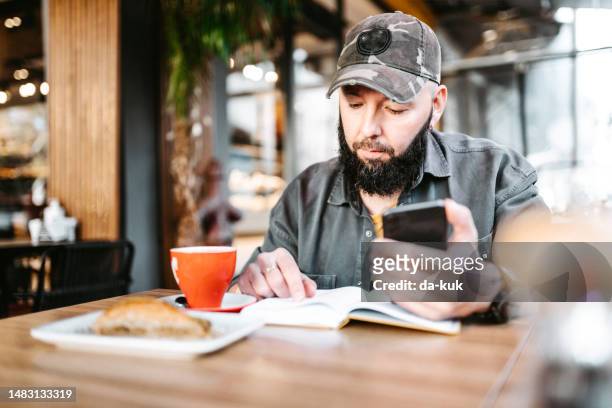 morning coffee and dessert before work. casual man using phone and note pad sitting in cafe - café da internet stock pictures, royalty-free photos & images