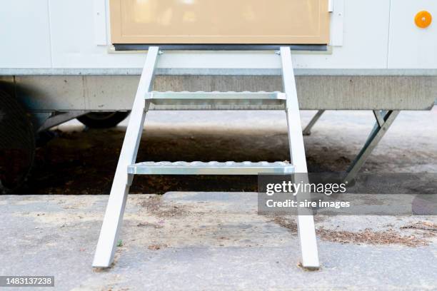 patterned metal ladder in front of a beige door of a camping trailer on a dirt floor, paris, also denoting a wheel. - winkelwagen stock-fotos und bilder