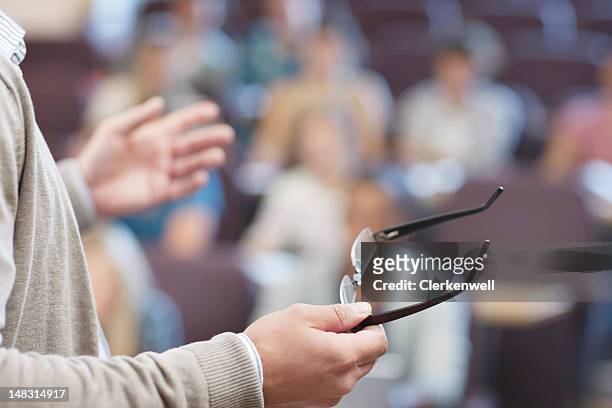 professor holding eyeglasses and gesturing in lecture hall - docent stockfoto's en -beelden