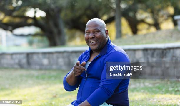 mature african-american man at park, pointing at camera - fat man sitting stock pictures, royalty-free photos & images