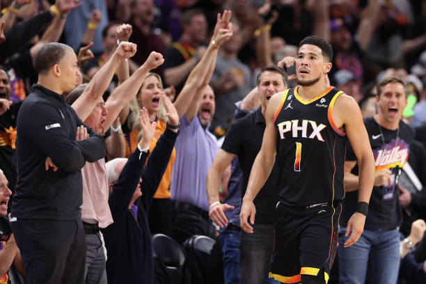 Devin Booker of the Phoenix Suns reacts after hitting a three-point shot ahead of head coach Tyronn Lue of the LA Clippers during the first half of...