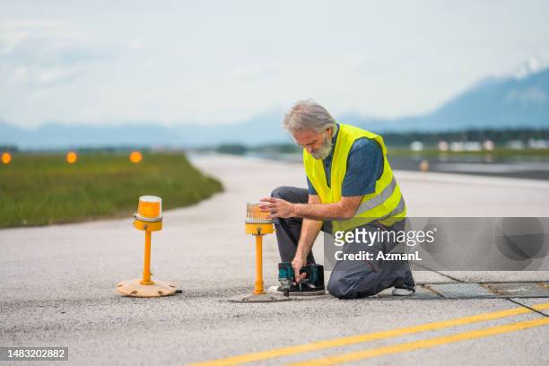airport maintenance crew member changing elevated lights on a runway - airport ground crew uniform stock pictures, royalty-free photos & images