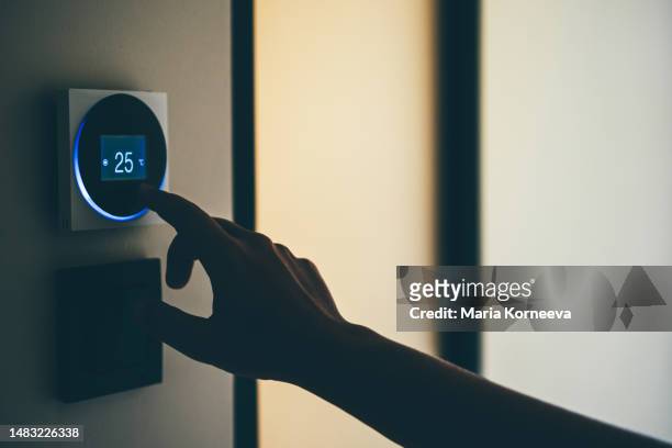 woman adjusts thermostat. woman adjusting temperature on smart thermostat at home. - air conditioner interior wall stock pictures, royalty-free photos & images