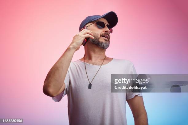 man wearing casual clothing, t-shirt and a cap using smart phone in front of colorful background - fashion in an age of technology costume institute gala after parties stockfoto's en -beelden