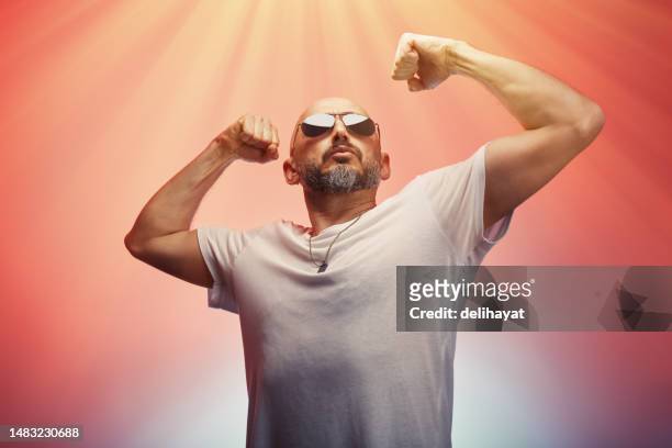 mann, der seine arme, muskeln und bizeps anspannt, zeigt seine stärke und männliche kraft, bunter hintergrund - siegerpose stock-fotos und bilder
