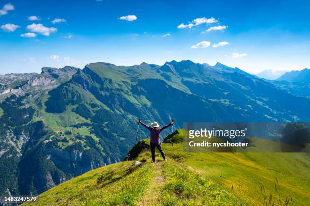 switzerland travel - mature asian woman with arms outstretched enjoying a beautiful summer day on the top of mannlichen in the swiss alps - jungfraujoch stockfoto's en -beelden
