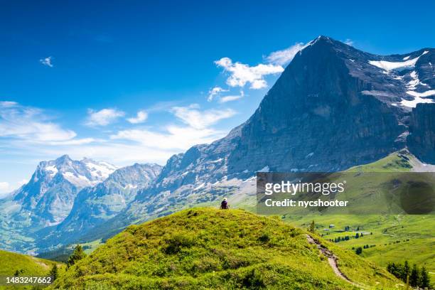 switzerland travel - female hiker sitting on small hilltop enjoying the views of the eiger mountain - mannlichen stock pictures, royalty-free photos & images