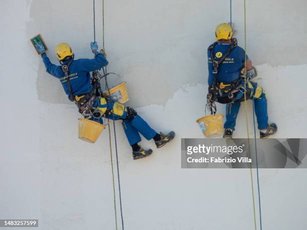 Detail of two acrobatic workers working on the wall of a building to be refurbished, hanging from a rope, many metres high on April 19, 2023 in...