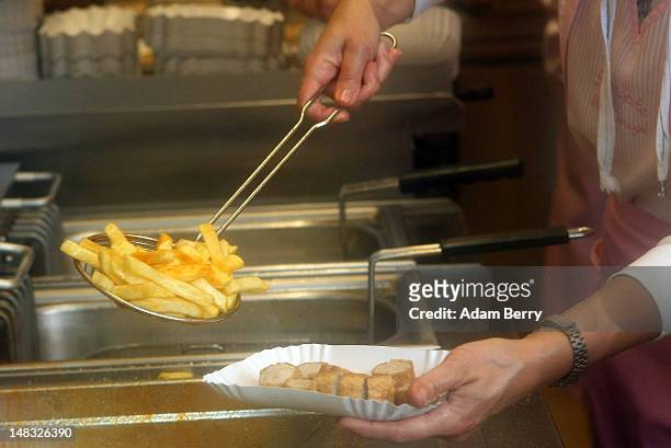 An employee prepares a plate of currywurst with french fries at Konnopke's currywurst stand on July 14, 2012 in Berlin, Germany. Currywurst,...