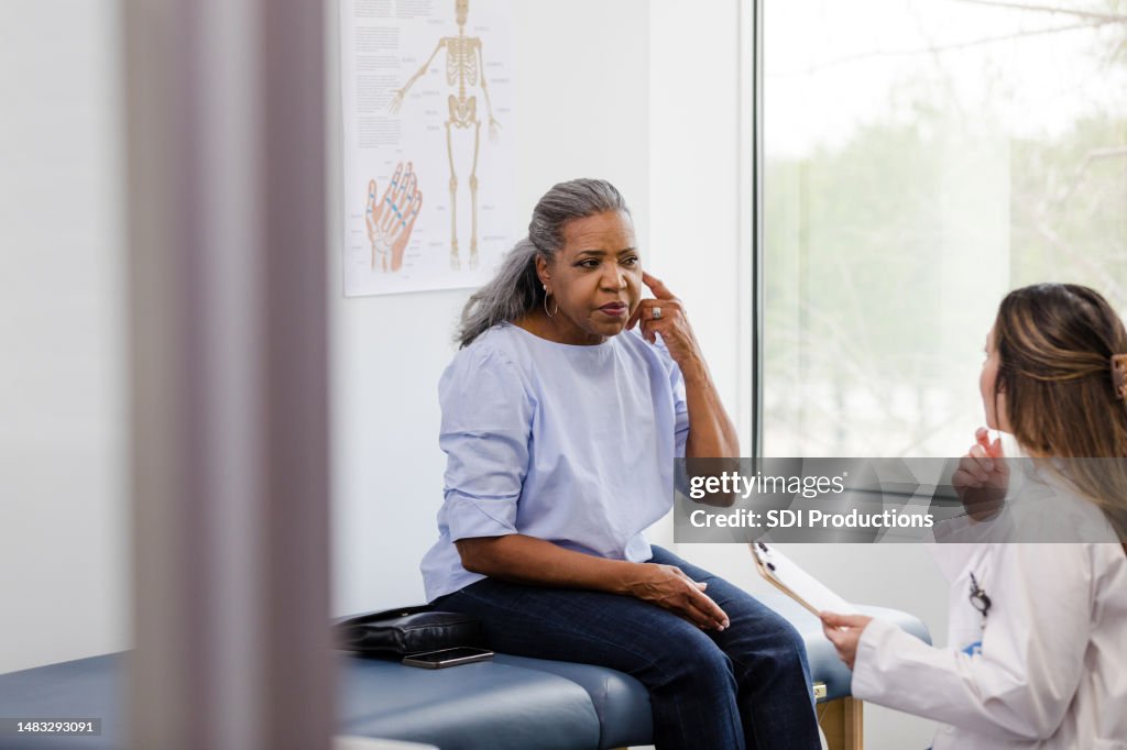 Paciente femenina señala la oreja mientras discute los síntomas con el médico