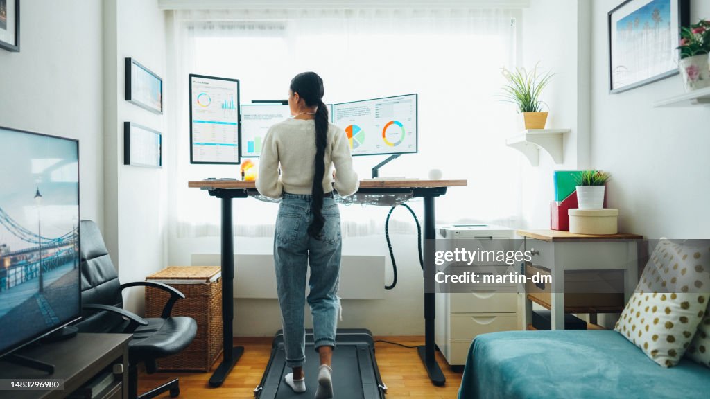 Woman at home office is walking on under desk treadmill