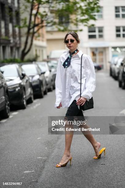 Emy Venturini wears black circle sunglasses from Ray Ban, gold earrings, a black with pale blue small and large polka dots print pattern silk small...