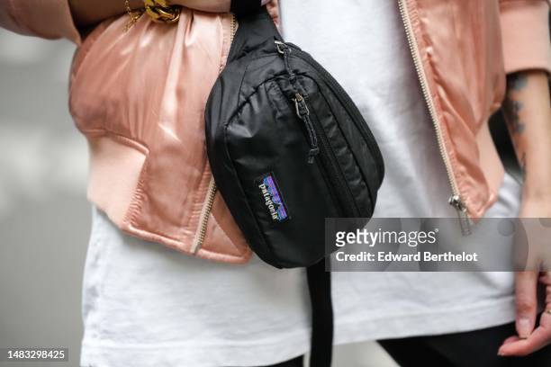 Emy Venturini wears a white long t-shirt from Uniclo, a pale pink shiny satin silk zipper bomber jacket, a black shiny silk fanny pack bag from...