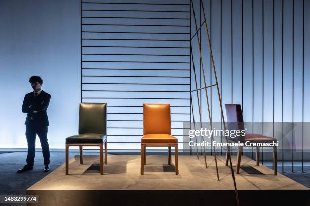 Man stands next to three chairs part of the design exhibition “Il potere dell’essenziale” by Hermes at La Pelota Jai Alai, Brera district, on April...