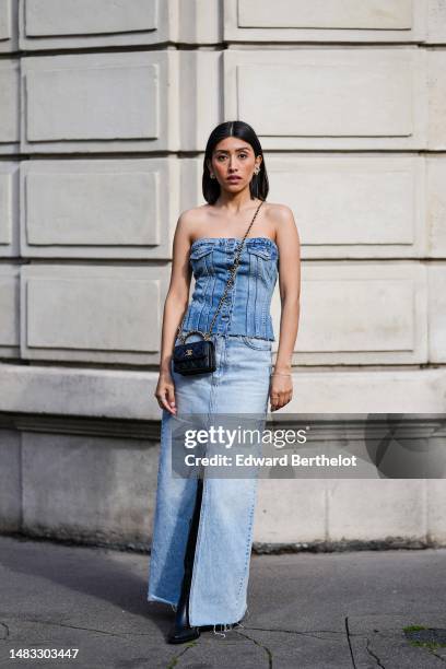 Angela Gonzalez wears gold earrings, a blue faded denim shoulder-off/ buttoned ripped corset top, a black shiny leather small Coco Handle handle...