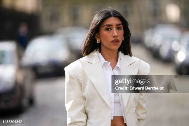 Angela Gonzalez wears gold earrings, a white cropped shirt, a white ribbed cropped tank-top, a white latte buttoned oversized / shoulder-pads blazer...