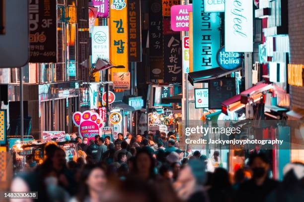 people walking among buildings on an illuminated street at night illuminated buildings and city street at night - séoul photos et images de collection