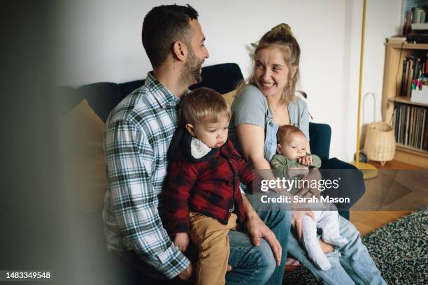 young family sitting together in lounge smiling - babyhood stock pictures, royalty-free photos & images