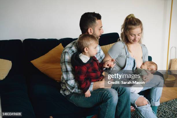 young family at home on sofa. mum looks down at newborn baby as he feeds - babyhood stock pictures, royalty-free photos & images