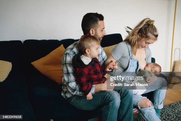 young family at home on sofa. mum looks down at newborn baby as he feeds - babyhood stock pictures, royalty-free photos & images