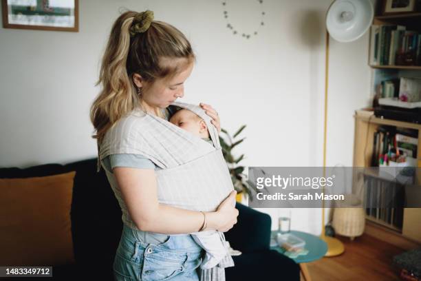 young mum looks down at newborn baby in sling - babyhood stock pictures, royalty-free photos & images