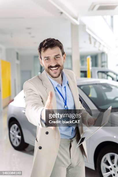 portrait of a professional salesman in car dealership reaches out to shake the customer's hand - customer success stock pictures, royalty-free photos & images