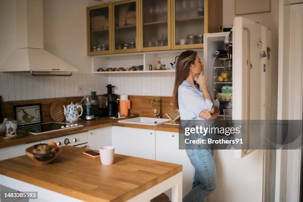 young woman searching food inside a refrigerator at home - refrigerator stock pictures, royalty-free photos & images