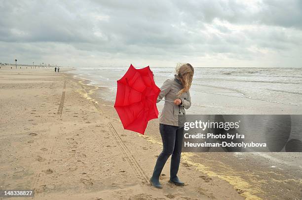 young woman with broken red umbrella - overcast beach stock pictures, royalty-free photos & images