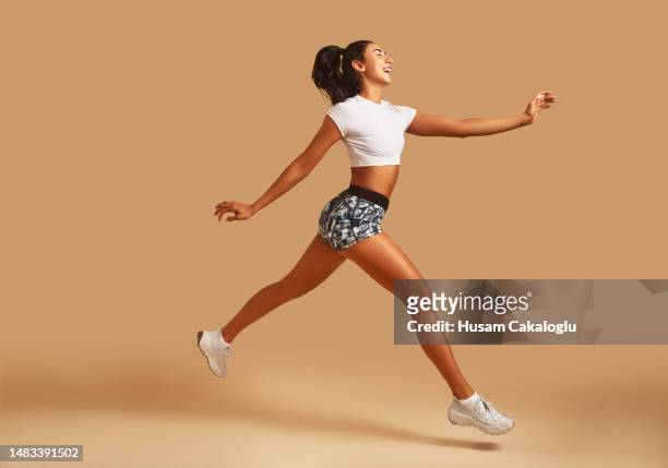 young athletic woman in sportswear running in front of brown background. - roupa desportiva imagens e fotografias de stock