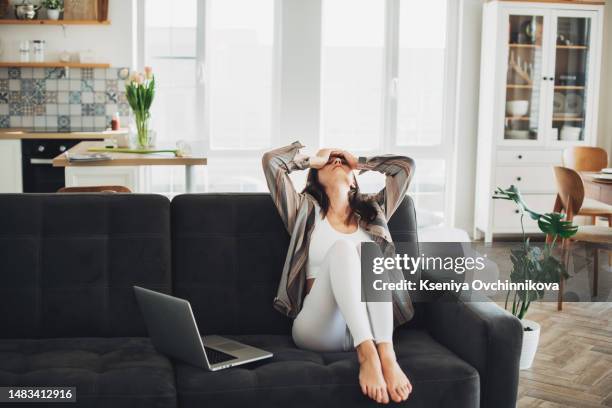 depressed young woman sitting on sofa at home - bedauern stock-fotos und bilder