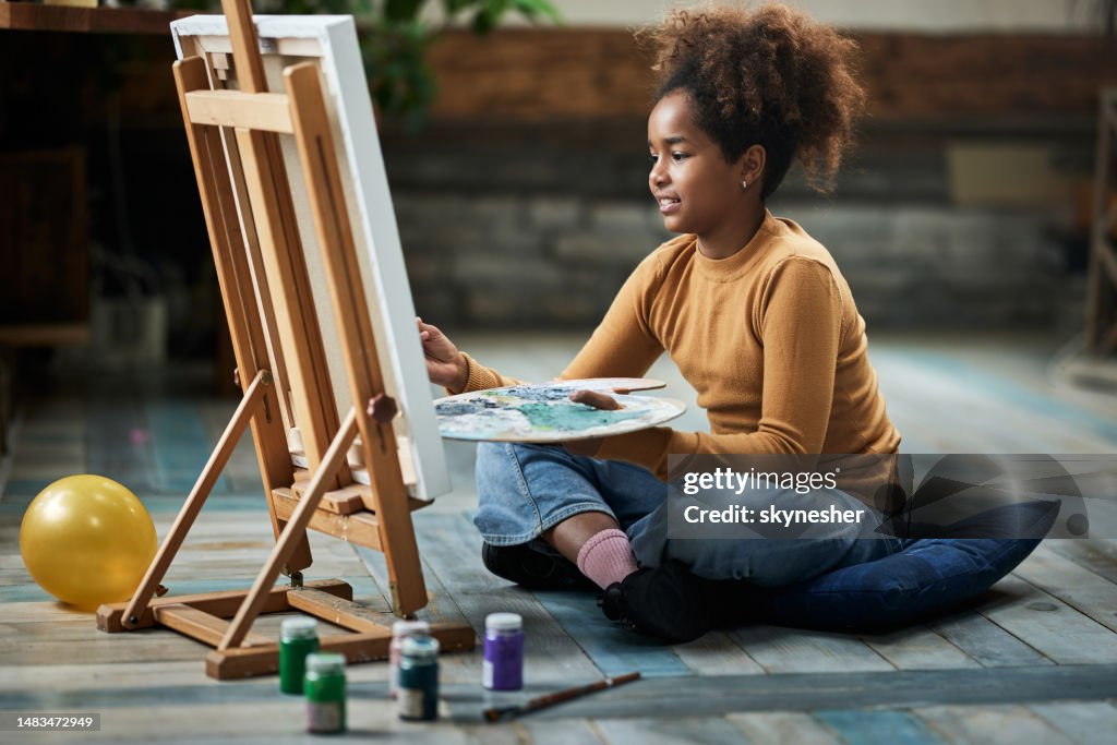 Glückliches afroamerikanisches kreatives Mädchen, das zu Hause malt.