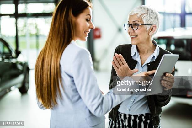 happy senior salesperson and her customer using touchpad in a car showroom. - touchpad bildbanksfoton och bilder