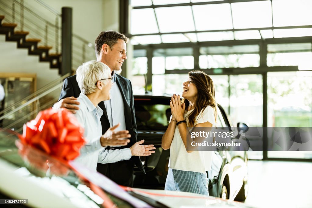 Alegre hija adulta sintiéndose sorprendida mientras sus padres le compraban un coche en una sala de exposición.