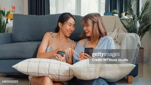 jeune belle couple lesbien asiatique dames s’amusant à utiliser un smartphone et à se détendre sur un canapé ensemble dans le salon à la maison. mois de la fierté, mois de la fierté axée sur le mode de vie. - phone credit card photos et images de collection